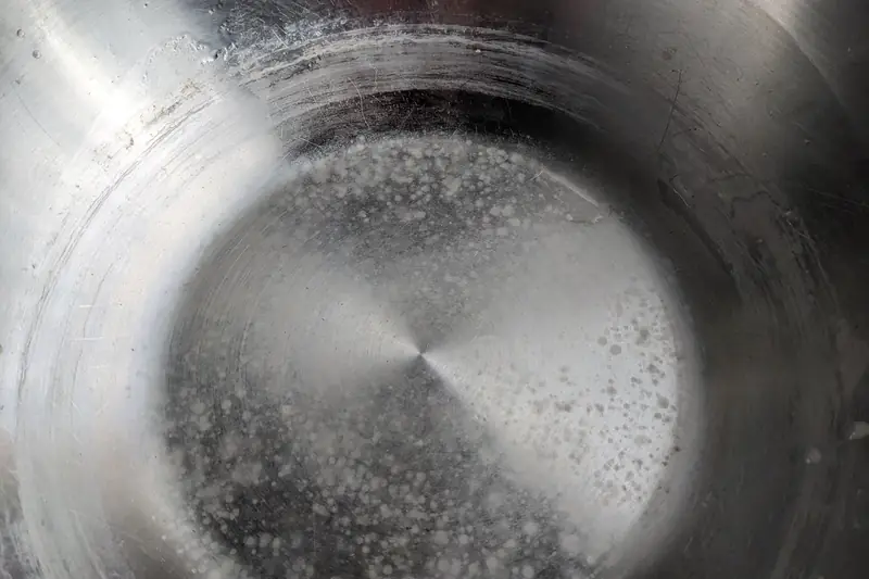The base of a stainless steel pot crusted with chalky white rings and spots left by boiled hard water