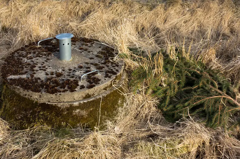 A single round concrete septic tank cover sitting in dry, tan grass