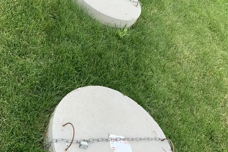 Two raised round concrete septic tank lids lying on a lawn, the nearer one chained and padlocked