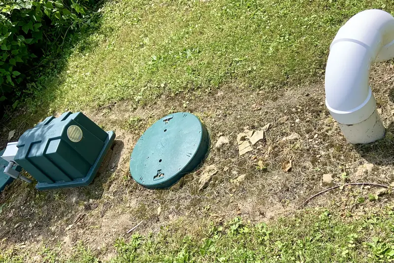 Two green septic riser covers propped open beside a white vent stack on a sloping lawn
