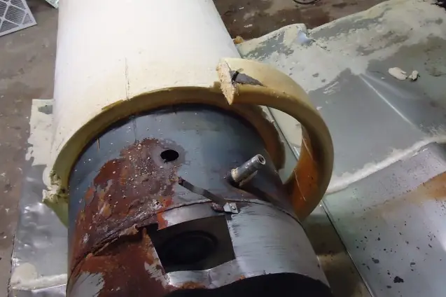 An old water heater with its outer jacket stripped away, showing the rust-streaked steel tank underneath
