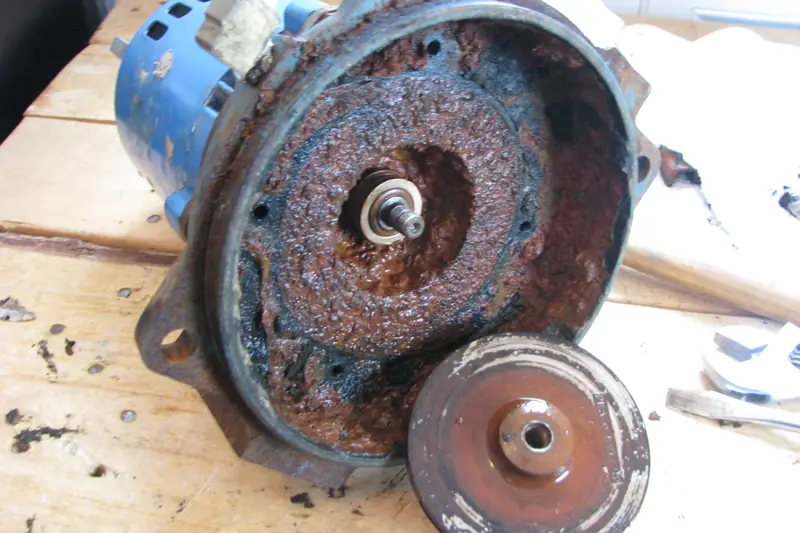 A pump taken apart on a wooden bench, its housing and impeller covered in brown rust and corrosion
